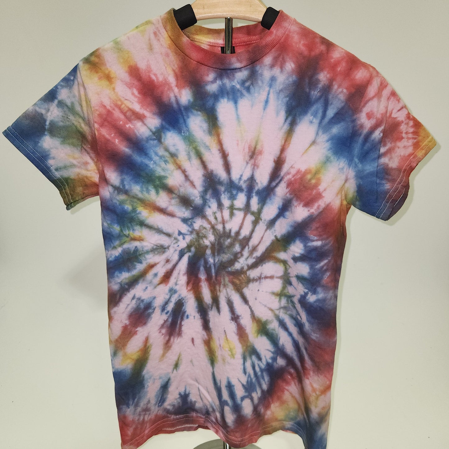 Tie-dye shirt on a hanger against a plain background